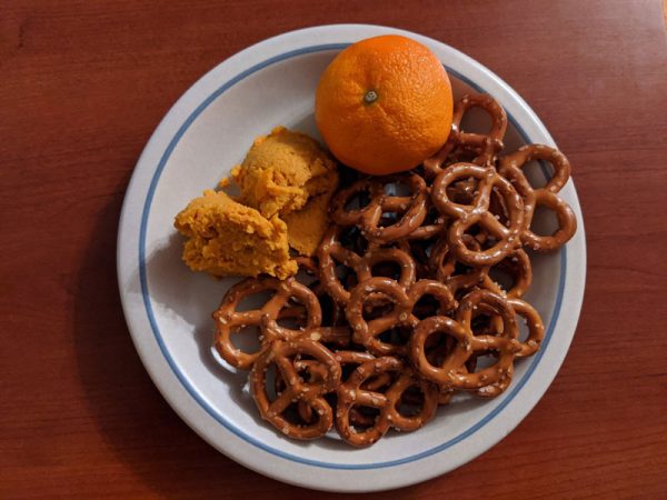 A plate with carrot and clementine humus, some mini pretzels, and a clementine